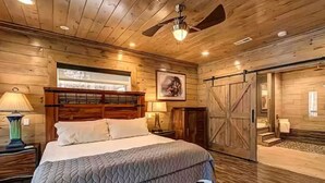 Une chambre aux murs lambrissés, avec un lit, un ventilateur de plafond et une grande fenêtre.