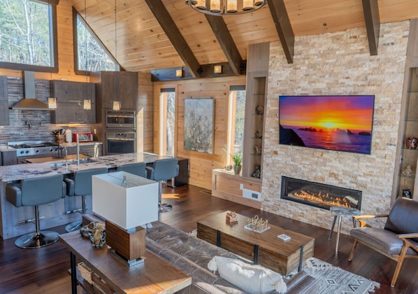 A spacious living area with a fireplace, a kitchen, and a dining area with modern furniture. - Stardust mountain cabin—upscale hideaway for two! (Sevierville)