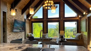 Une cuisine dotée d’un grand îlot central, de sièges intégrés et de grandes fenêtres offrant une vue sur les montagnes.