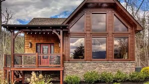 Une cabane en bois avec des fondations en pierre, de grandes fenêtres et une terrasse en bois.