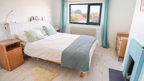 A bedroom with a bed, a nightstand, a dresser, a window with curtains, and a radiator. - Seashells - 4 Bed - 2 Bath - Nr Beach - Sleeps 7 (Isle of Wight)