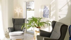 A modern living room with two grey armchairs, a white floor, a large window, and a potted plant. - Seashells - 4 Bed - 2 Bath - Nr Beach - Sleeps 7 (Isle of Wight)
