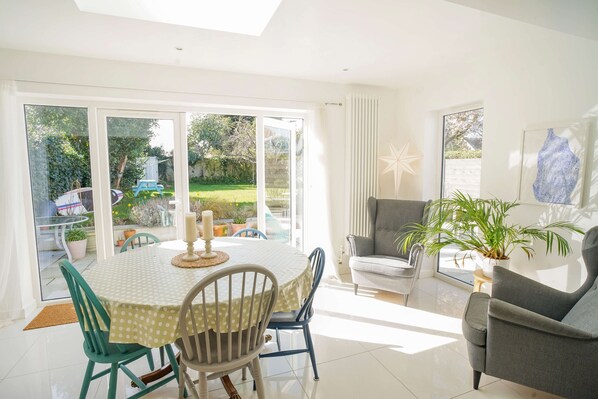 A bright, sunlit room with a dining table, chairs, and a sofa.