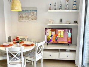A dining area with a round table, white chairs, and a television displaying animated characters.