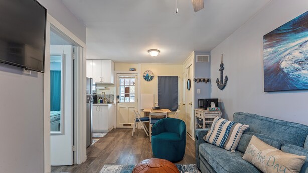 A living room with a blue sofa, a brown ottoman, and a kitchen in the background.