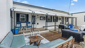 A covered patio area with outdoor seating, a grill, and a blue trash bin.