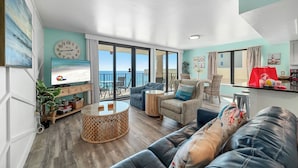 Un salon spacieux avec une grande télévision, des sièges confortables, un balcon avec vue et un coin cuisine.