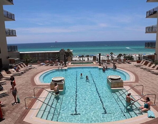 Relax by the resort pool, surrounded by lounge chairs and sunbeds, with a clear view of the ocean.