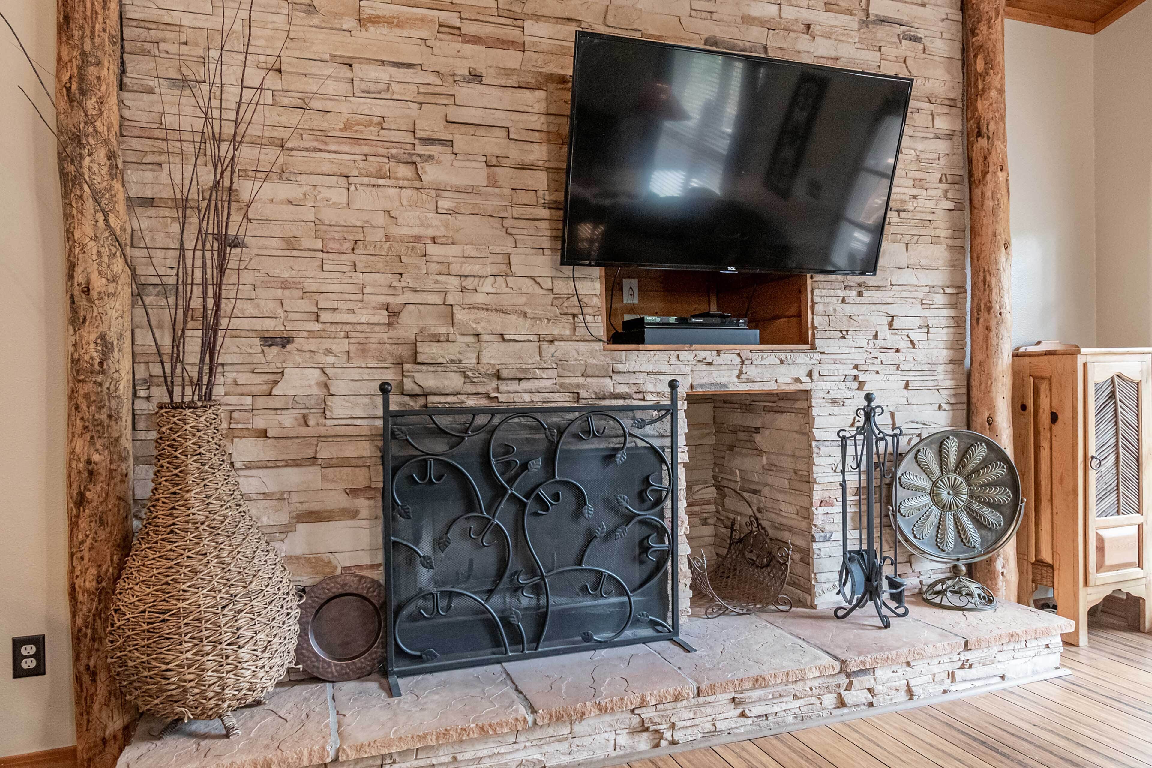A stone fireplace with a TV mounted above it, a decorative metal screen, and a fan to the right.