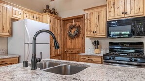 A kitchen with wooden cabinets, a stainless steel sink, a white refrigerator, a black microwave, and a stove.