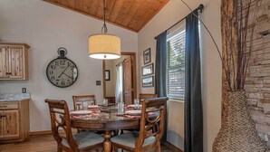A dining area with a wooden table, chairs, a wall clock, and a hanging light fixture.