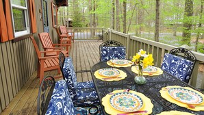 Eine Holzterrasse mit Sitzgelegenheiten im Freien, darunter Stühle und ein Tisch, gedeckt mit Tellern und einer Blumenvase.