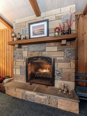 A stone fireplace with a framed picture above it, a shelf with decorative items, and a log fire burning.