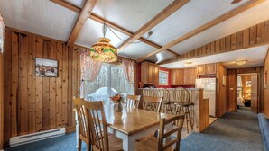 Ein Holzinterieur mit Esstisch, Stühlen, einer Deckenleuchte und einer Küchenzeile.