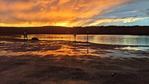 Blick auf einen See mit einer Bank und Informationsschildern bei Sonnenuntergang.