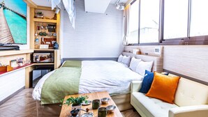 Habitación de hotel moderna con una cama, un sofá, una mesa de centro y un estante montado en la pared con varios objetos.