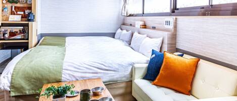 A modern hotel room with a bed, a sofa, a coffee table, and a wall-mounted shelf with various items.