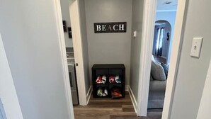 A hallway with a 'BEACH' sign, a shoe rack with colorful shoes, and a wooden floor.