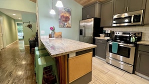 A kitchen with a granite countertop, stainless steel appliances, and a wooden ceiling. - Peaceful Forest Cottage with Hot Tub  Near Beach+Twin Rocks  Family&Pet Friendly (Rockaway Beach)