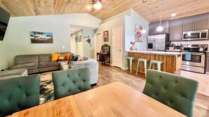 A modern kitchen with stainless steel appliances, a dining area with a wooden table and green upholstered chairs, and a ceiling fan. - Peaceful Forest Cottage with Hot Tub  Near Beach+Twin Rocks  Family&Pet Friendly (Rockaway Beach)