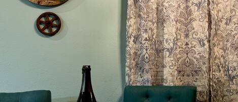 A dining table with a bottle of wine, two glasses, and a decorative plate with food. A wooden sign with a scenic route message is on the wall.