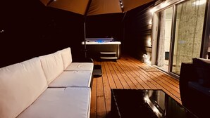 A covered outdoor area with a wooden deck, a white sofa, and a hot tub. - Peaceful Forest Cottage with Hot Tub  Near Beach+Twin Rocks  Family&Pet Friendly (Rockaway Beach)