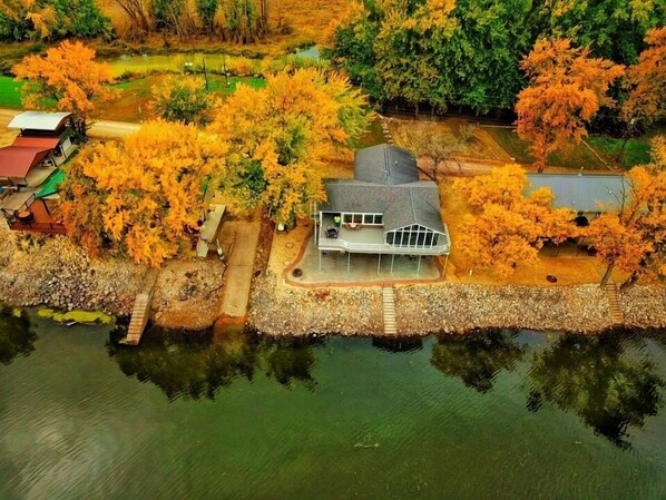 A house with a large deck, surrounded by autumn foliage and a body of water.
