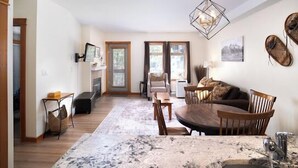 A dining area with a round table, chairs, a rug, a fireplace, and a hanging light fixture. - Beautiful 2 bedroom condo in the heart of the Rocky Mountains (Canmore)