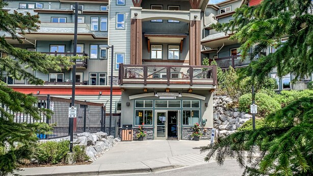A multi-story hotel with a prominent red roof, balconies, and a stone facade. - Beautiful 2 bedroom condo in the heart of the Rocky Mountains (Canmore)