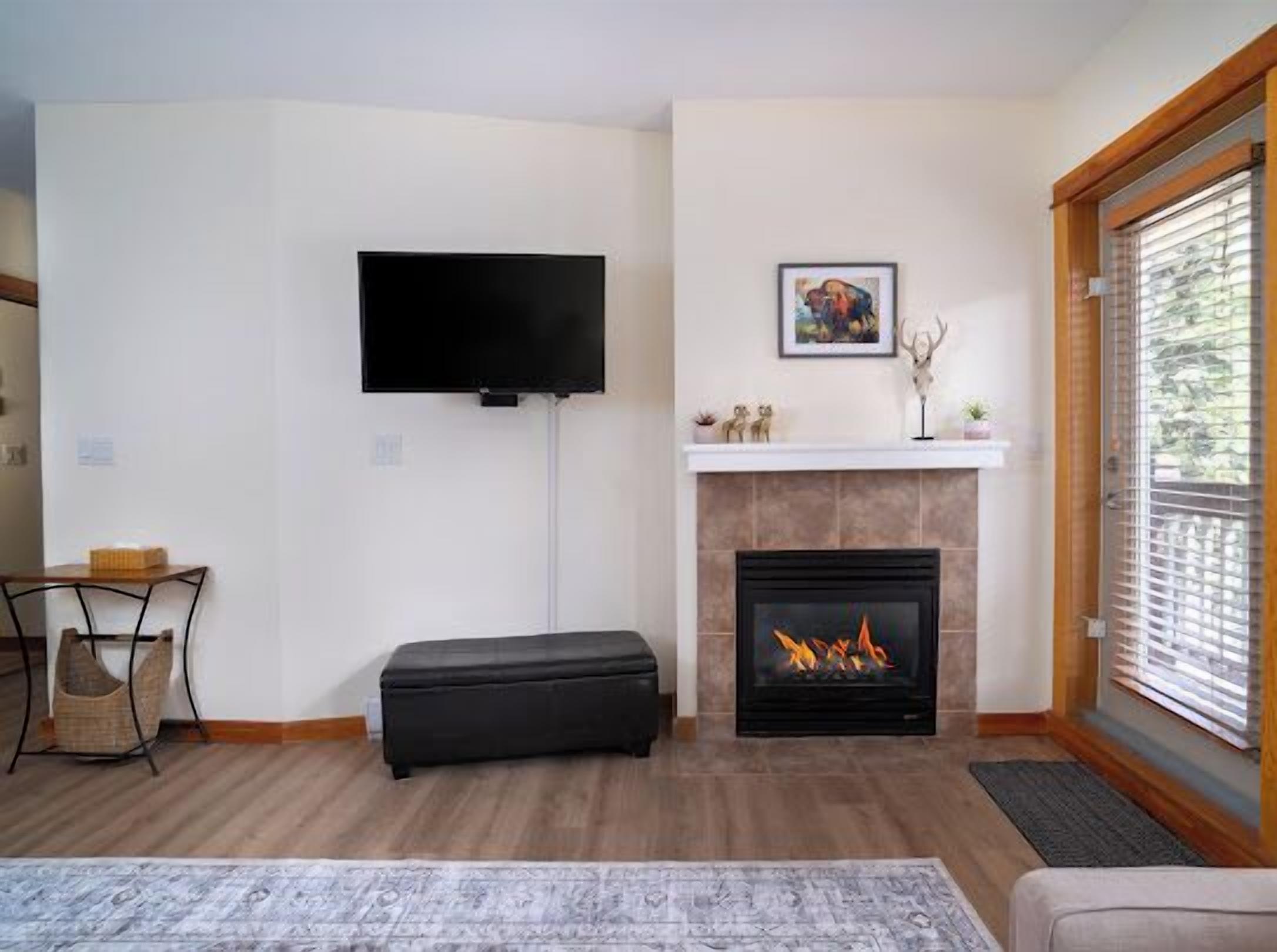 A living room with a flat-screen TV, a fireplace, a mounted picture, and a window with blinds.