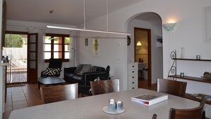 A dining area with a table, chairs, and a book. There is a black leather sofa and a patterned armchair in the background. - Sol i Vent - L'Estartit, Torre Vella (Estartit (L´))