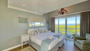 Une chambre avec deux lits, une table de chevet, une chaise, un lustre et une vue sur la mer.