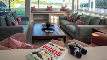 A modern living room with a large window, a sofa, a coffee table, and a book titled 'Birds by Colour'.