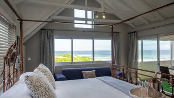 Ein Bett mit Baldachin und Blick auf den Ozean, ein Balkon mit Tisch sowie eine Champagnerflasche auf dem Bett.