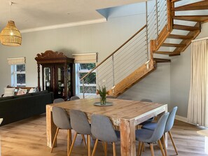 A dining area with a wooden table and chairs, a staircase, and a large window. - Beach Break Guest Houses and Villas (Cape Saint Francis)