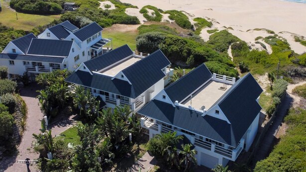 Una propiedad costera con varias casas, una playa y vistas al océano.