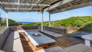 Un espacio de estar al aire libre con vistas al océano, una chimenea y una estructura de pérgola.