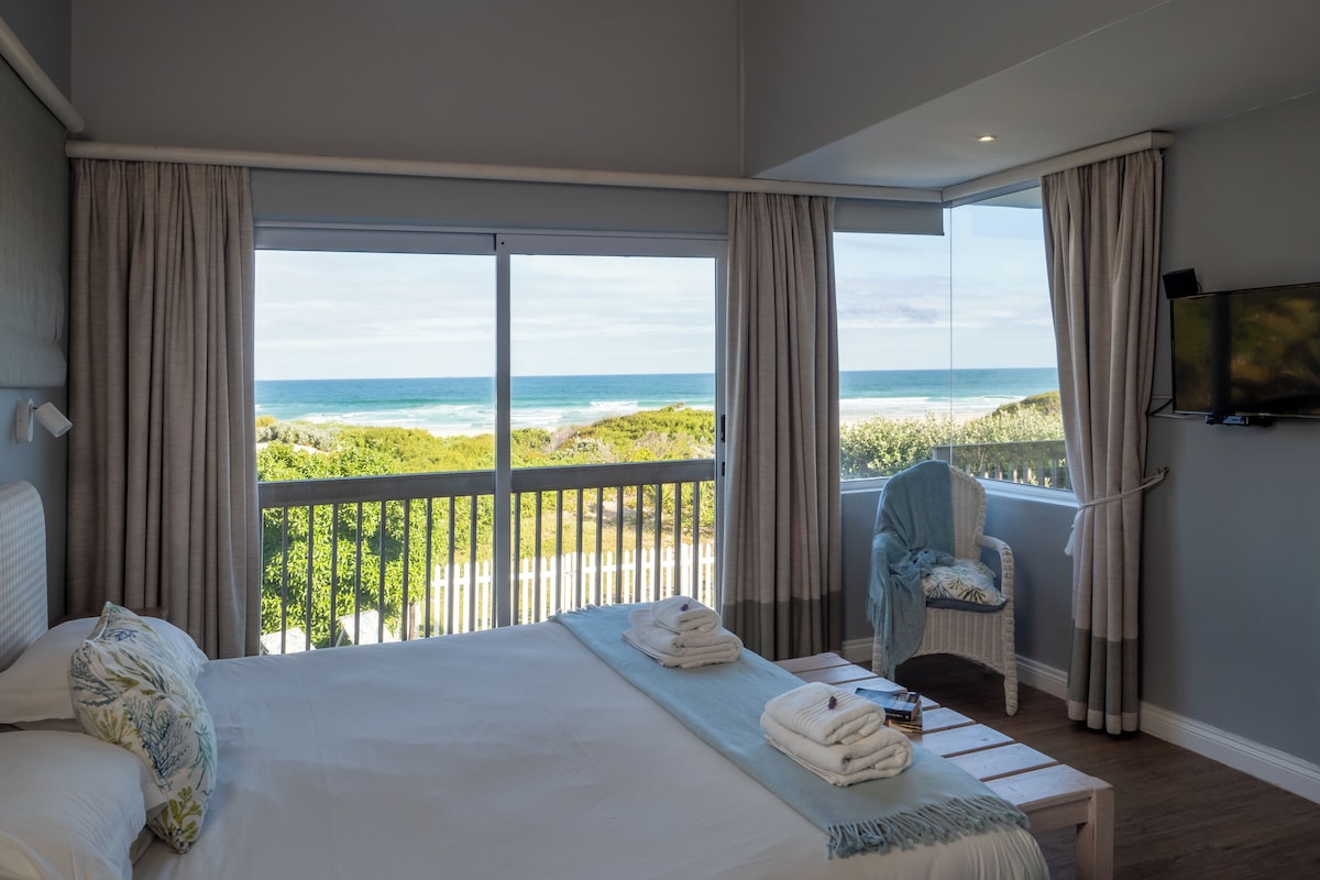 Ein Schlafzimmer mit Bett, Stuhl, Fernseher und einem Balkon mit Meerblick.