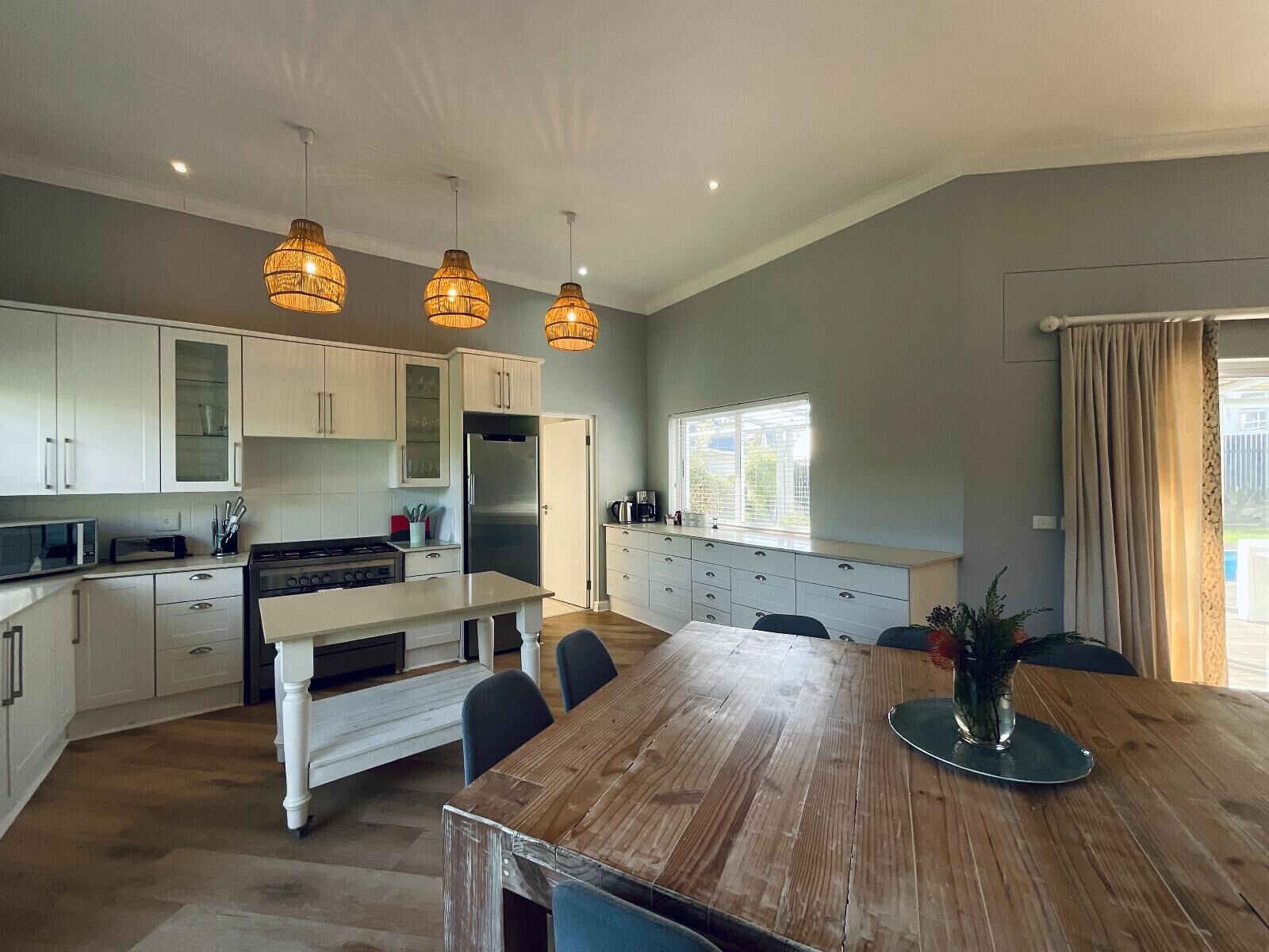 A modern kitchen with white cabinets, a wooden dining table, and pendant lighting.