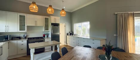 A modern kitchen with white cabinets, a wooden dining table, and pendant lighting.