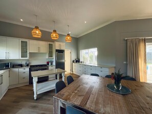Une cuisine moderne avec des meubles blancs, une table à manger en bois et des luminaires suspendus.