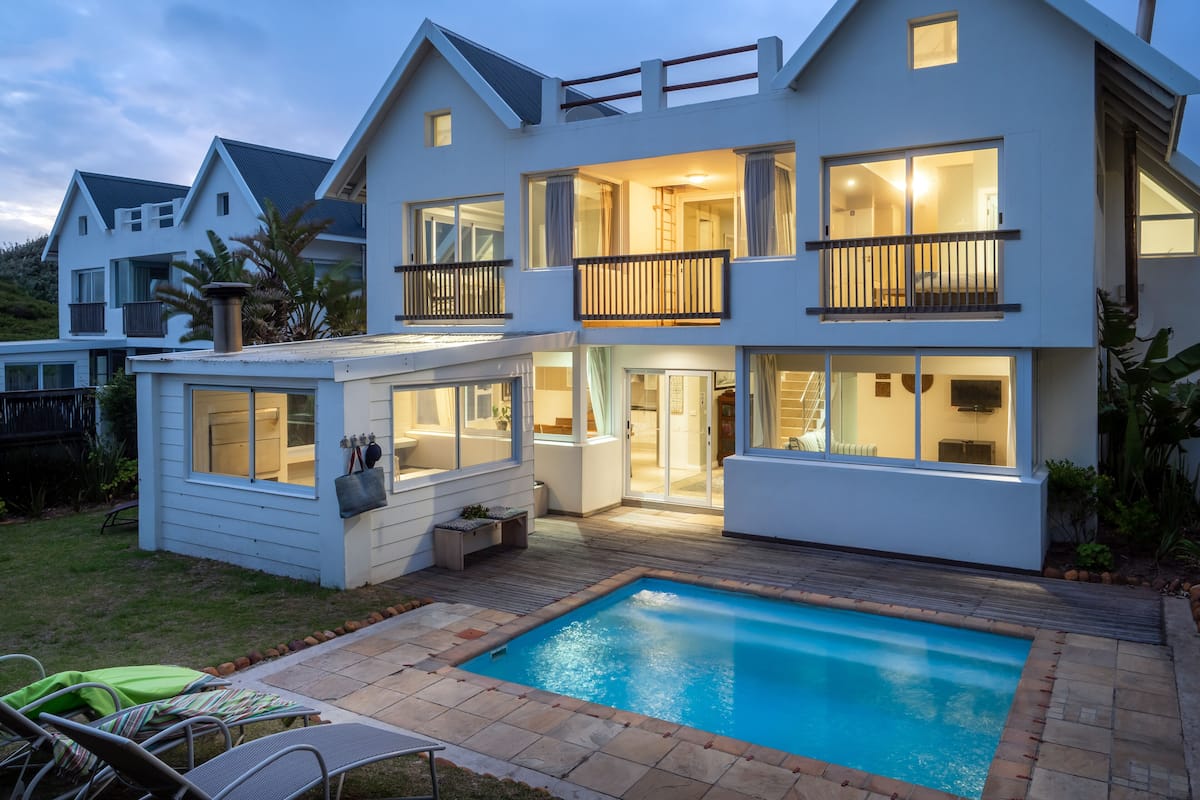 A modern two-story house with a swimming pool, large windows, and a balcony.