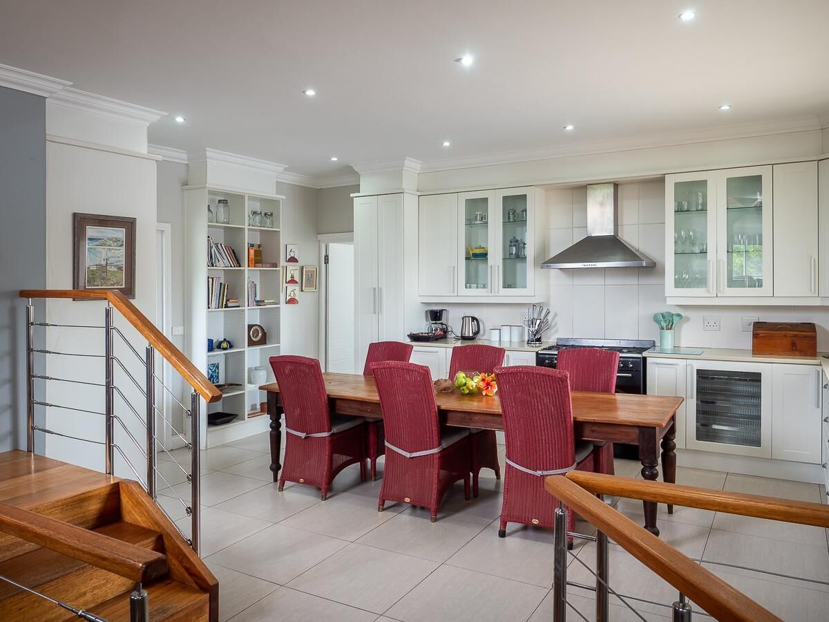 A modern kitchen with white cabinetry, a dining table with red chairs, and a staircase with wooden railings.