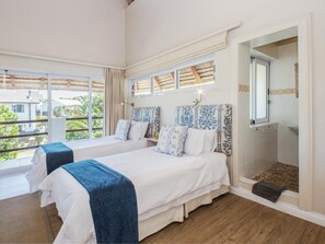 A hotel room with two beds, a large window, and a shower area.