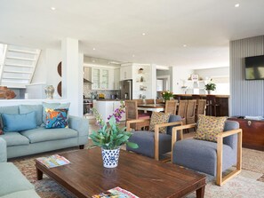Ein modernes Wohnzimmer mit einer Couch, Sesseln, einem Couchtisch und einem Essbereich mit Tisch und Stühlen.
