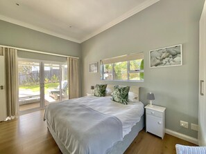 Un dormitorio con una cama grande, una mesita de noche, una ventana con vistas a la vegetación y un cerramiento de vidrio corredera que da a un espacio al aire libre.