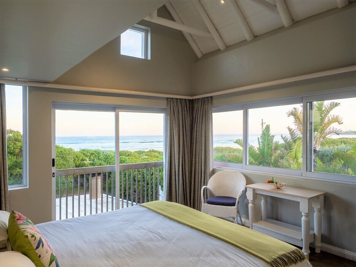 A bedroom with a large bed, a desk, and a view of the ocean.