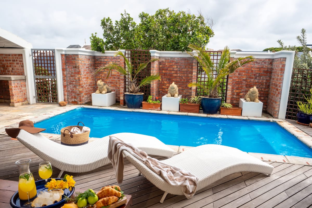 A poolside area with lounge chairs, a dining table with food and drinks, and potted plants.