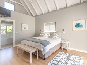 A bedroom with a bed, bench, bedside tables, and artwork. - Beach Break Guest Houses and Villas (Cape Saint Francis)