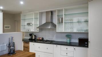 Una cocina moderna con armarios blancos, encimera negra y estantes de vidrio arriba.